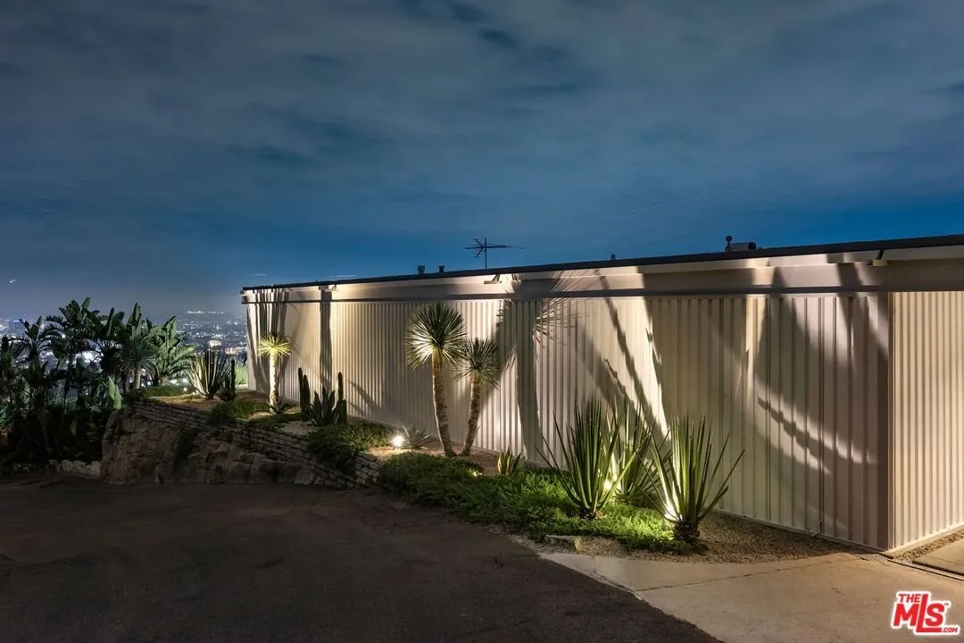 The corrugated steel elevation from the entry side at dusk, planting along the wall
