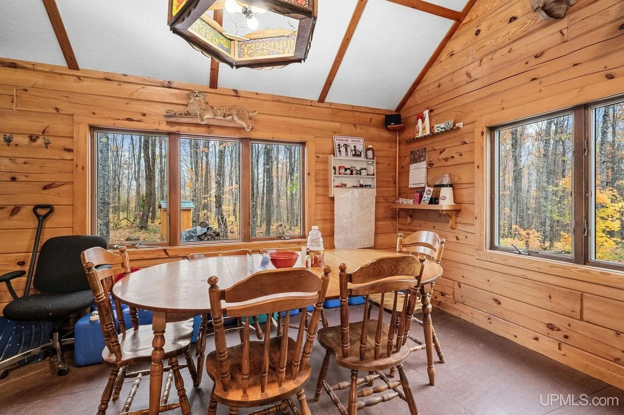 The dining table and chairs under the peaked pine ceiling, windows on two walls