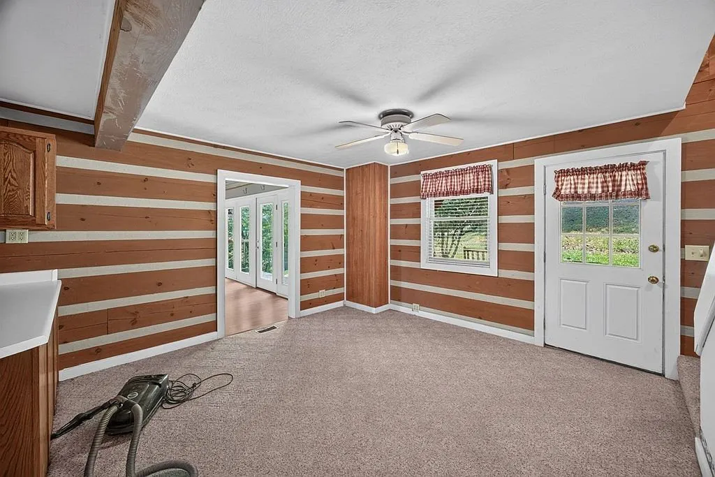 An open room with log-paneled walls, carpet and a ceiling fan