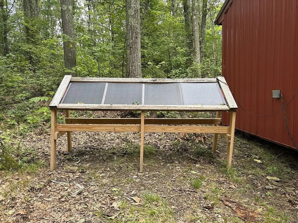 Four solar panels on a lumber frame beside the red shed