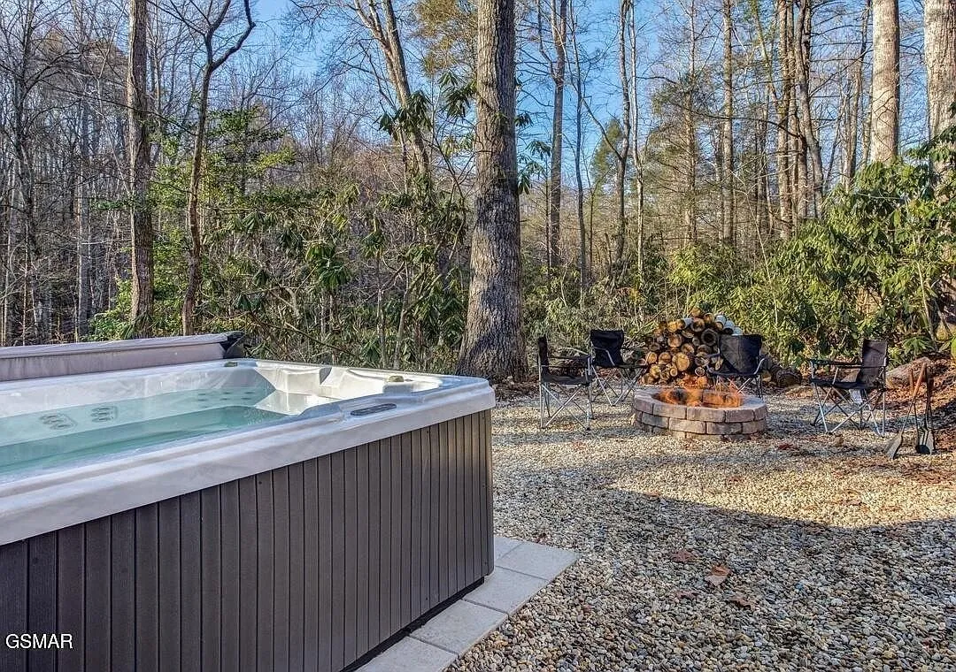 The hot tub on the gravel pad with stacked firewood behind it