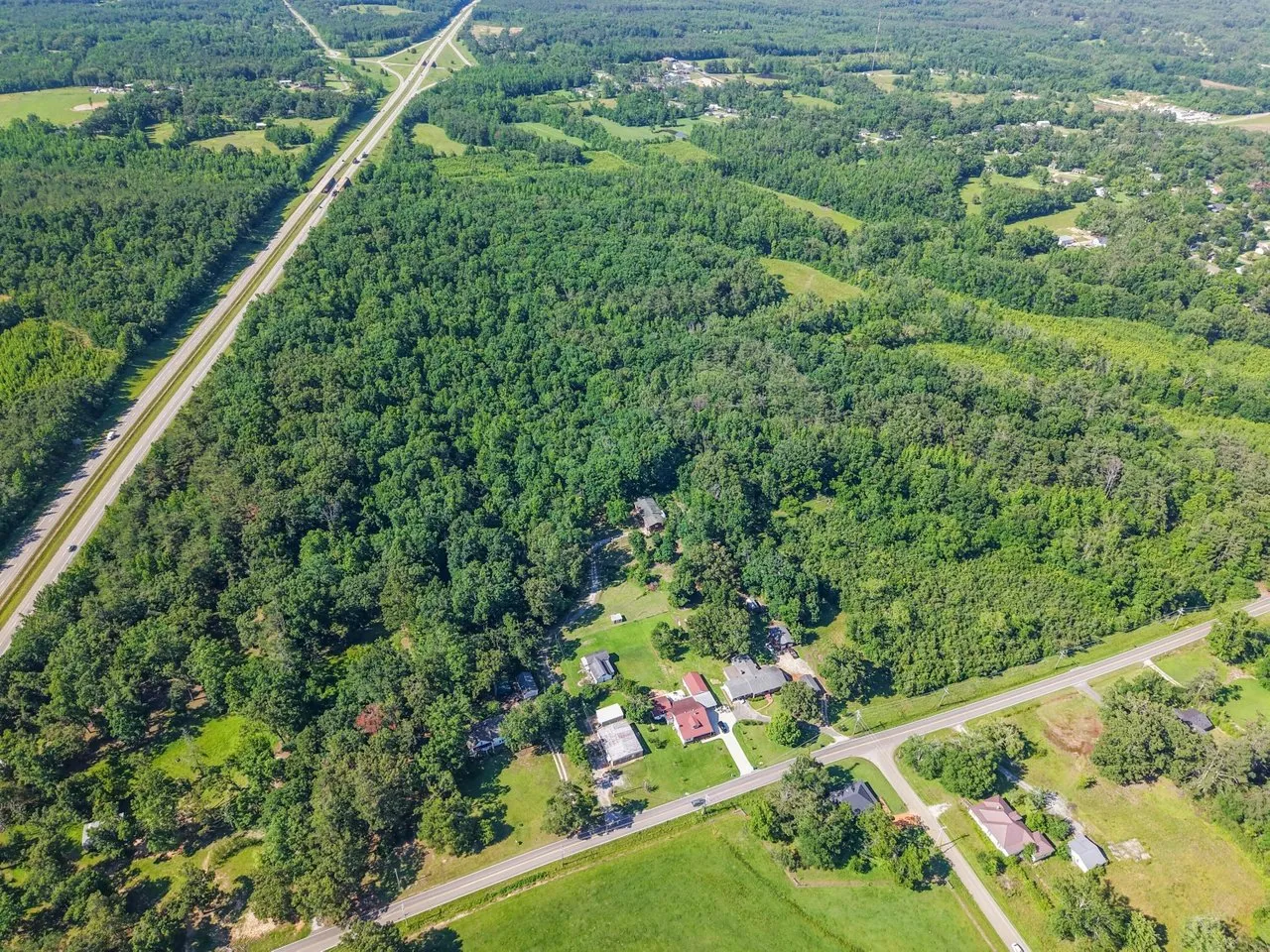 Aerial over the wooded acreage toward the road and the town beyond