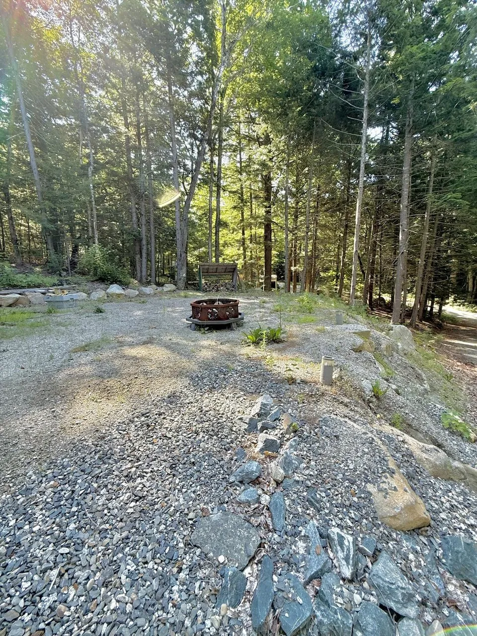 The gravel yard with the fire ring in the trees