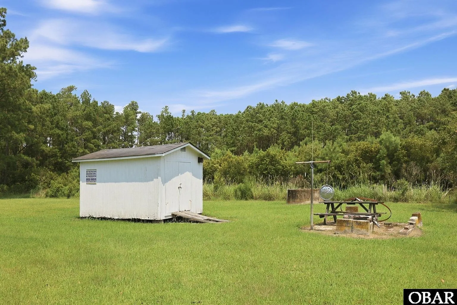 The white shed in the yard with a grill and picnic table beside it