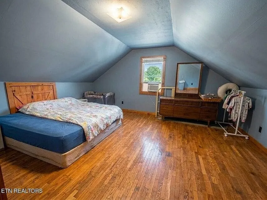An upstairs bedroom with a queen bed, sloped ceiling and a dresser with mirror