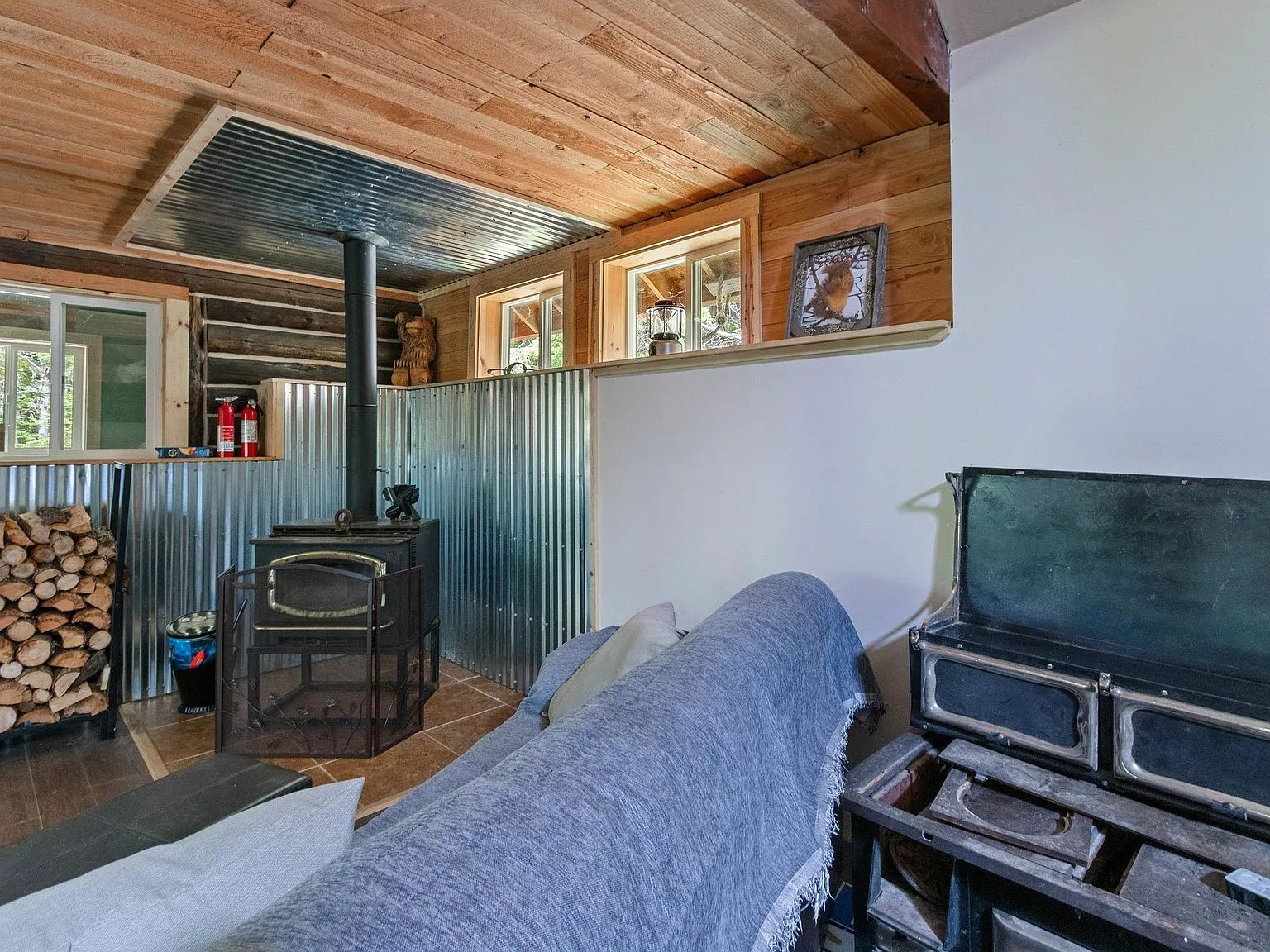 The wood stove and sofa seen from across the main room, with a loft ladder visible