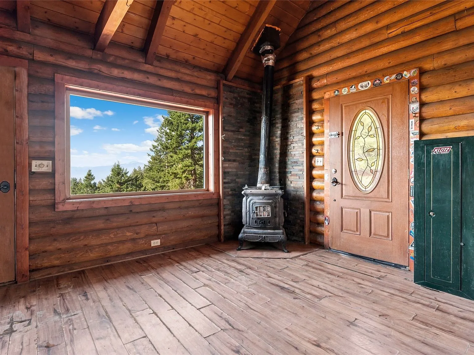 The main room with a wood stove, log walls and a window framing the trees
