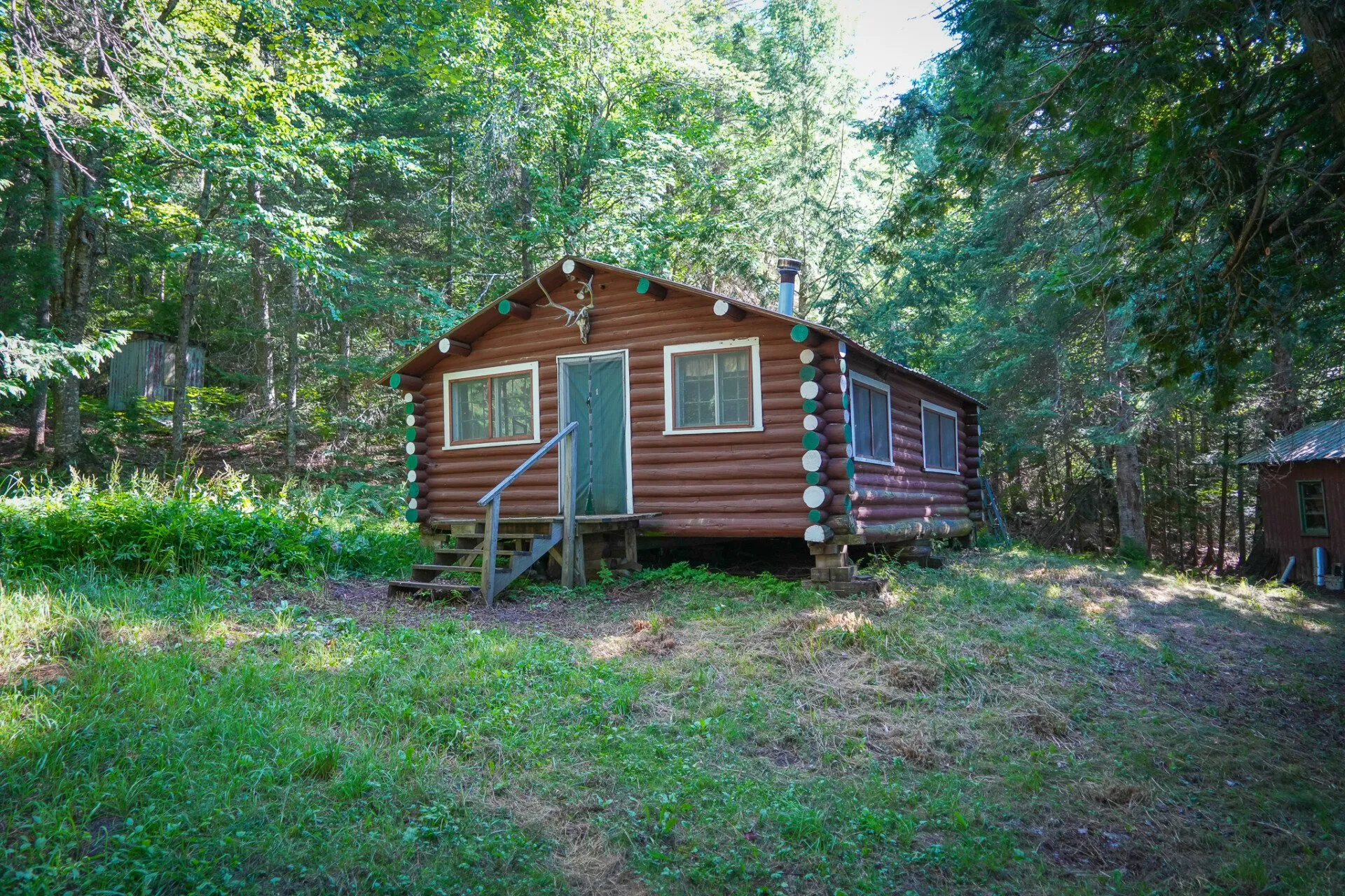 The second log cabin at the edge of a grassy clearing, a door and two windows