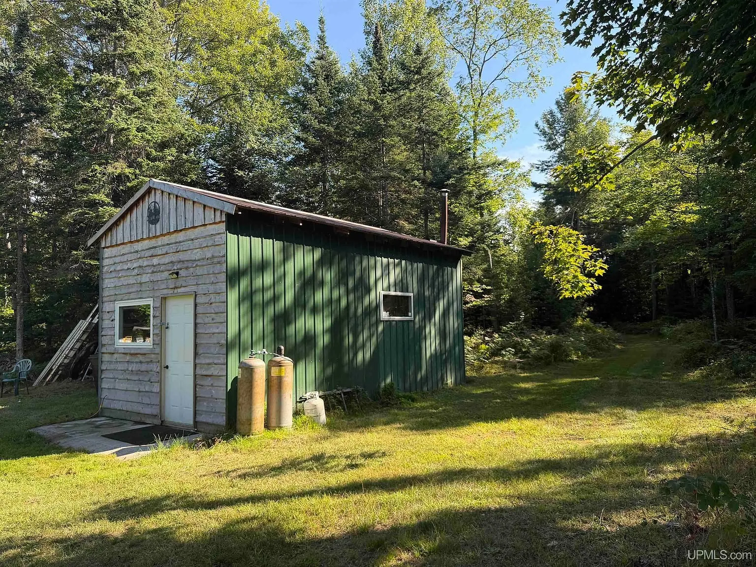 The side of the base camp with the green siding, the propane cylinders and the stove pipe