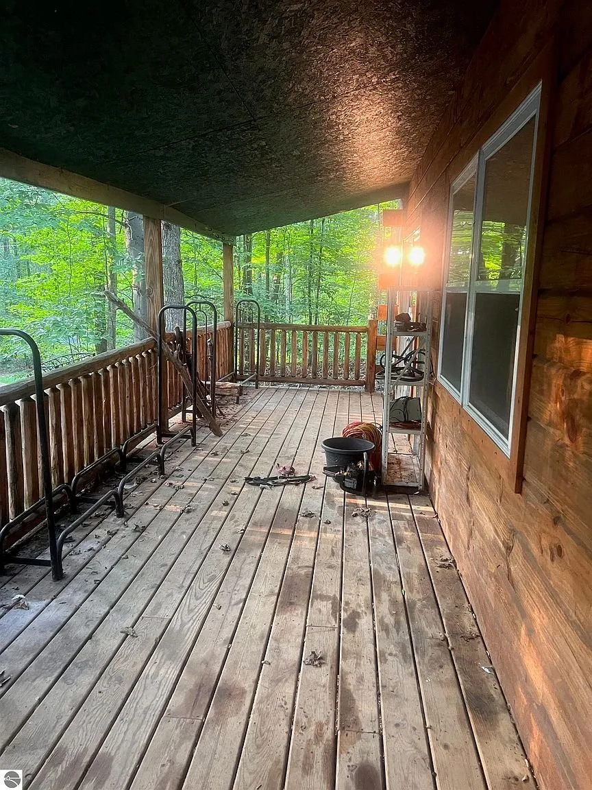 The covered porch with the bed frame, the rail and the woods beyond