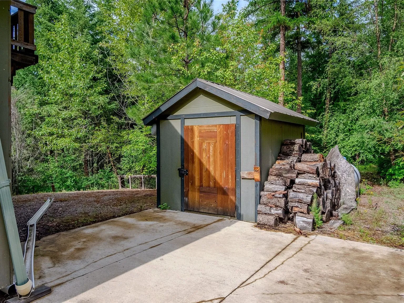 A storage shed with a woodpile stacked beside it