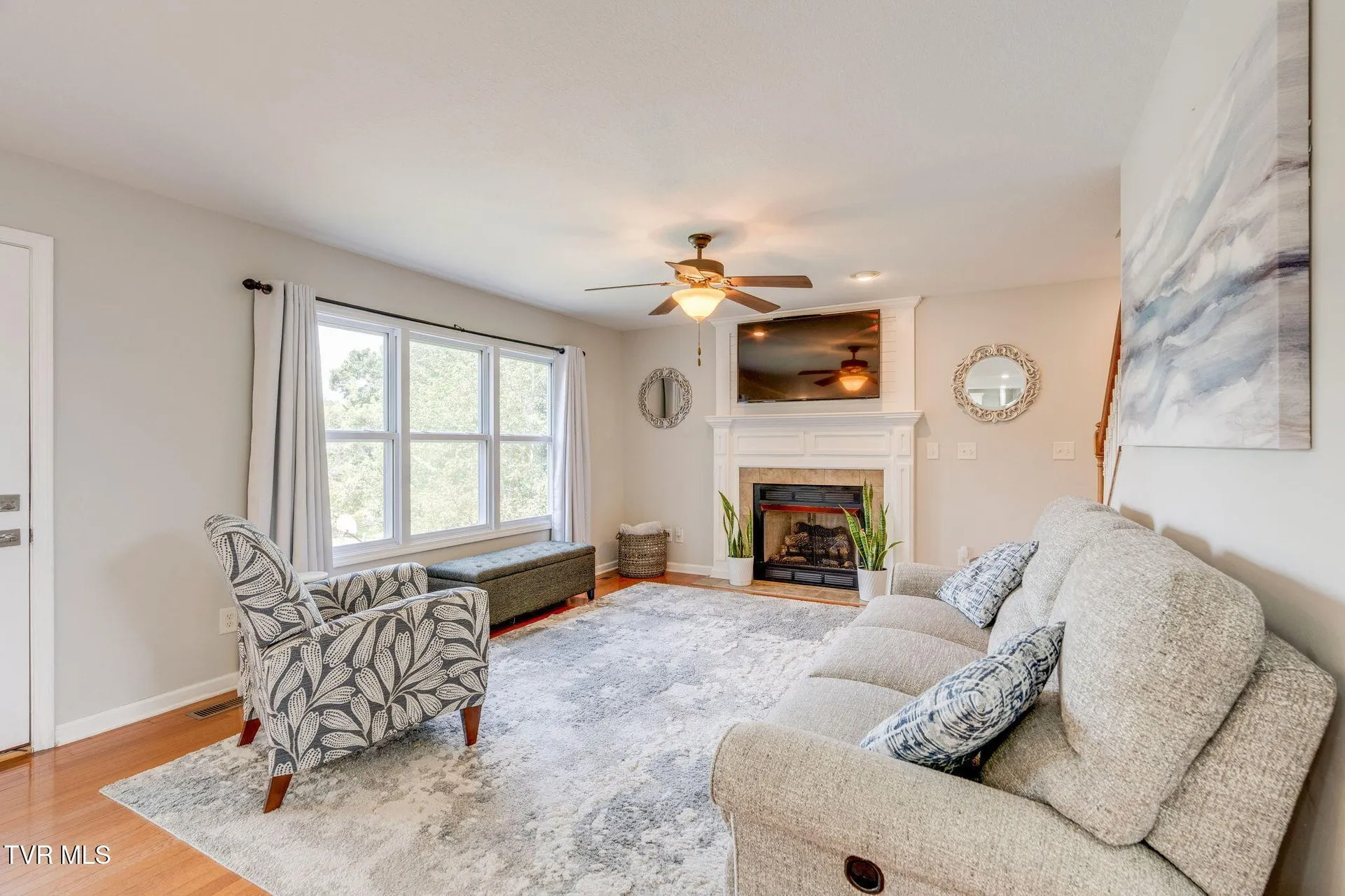 The family room with the fireplace, wide windows and a ceiling fan