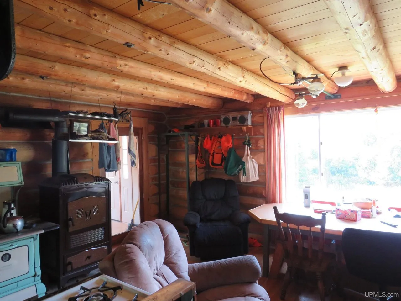 The main room from the kitchen end, wood stove, chairs and a bright window