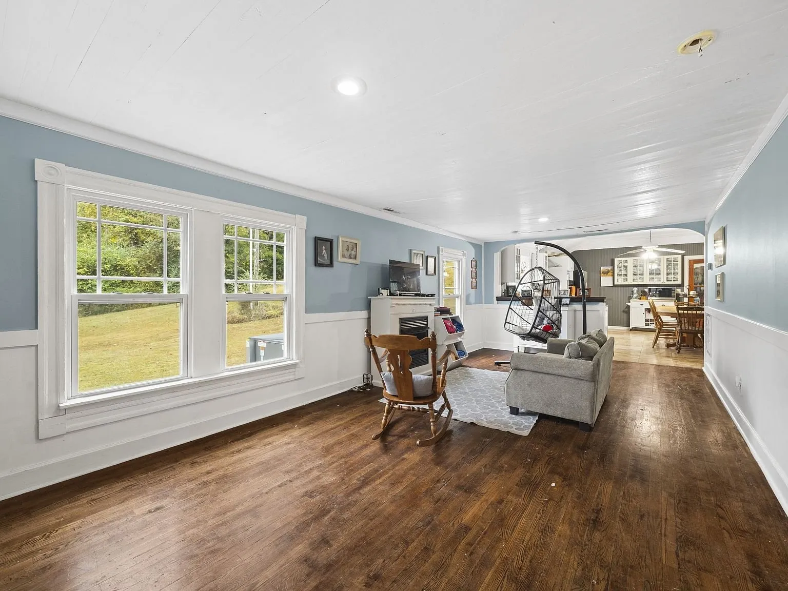Living room with refinished wood floors, wainscoting, and tall windows