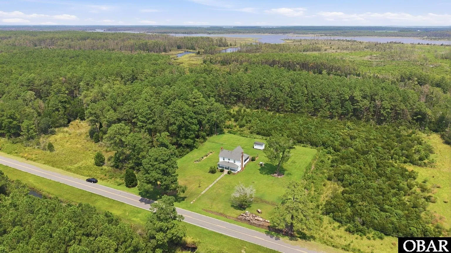 Aerial of the house and yard beside Loop Road with pines behind and water on the horizon