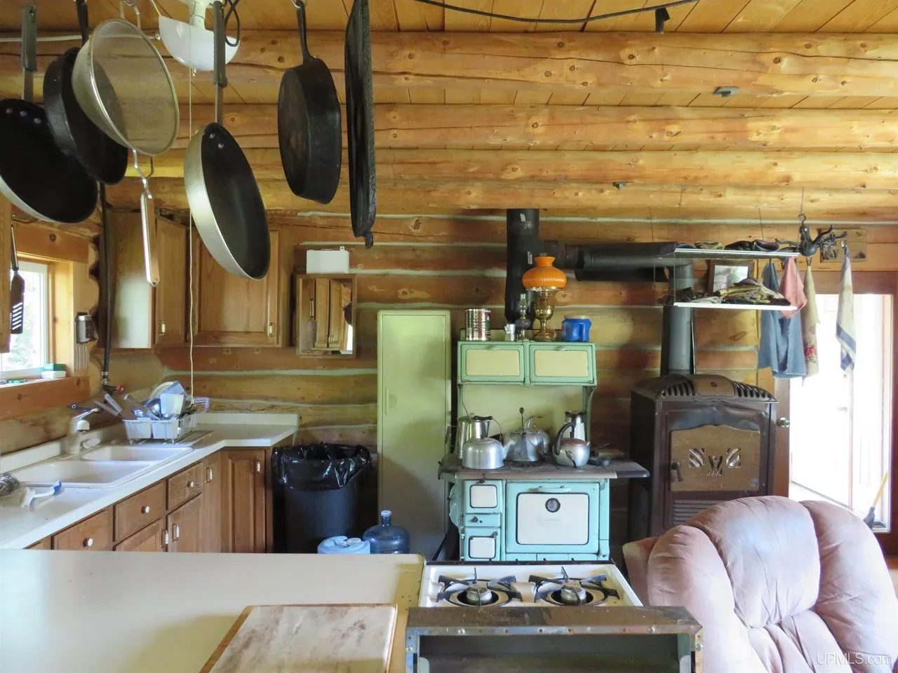 The kitchen with a green enamel wood cookstove, cabinets and cast iron on the wall
