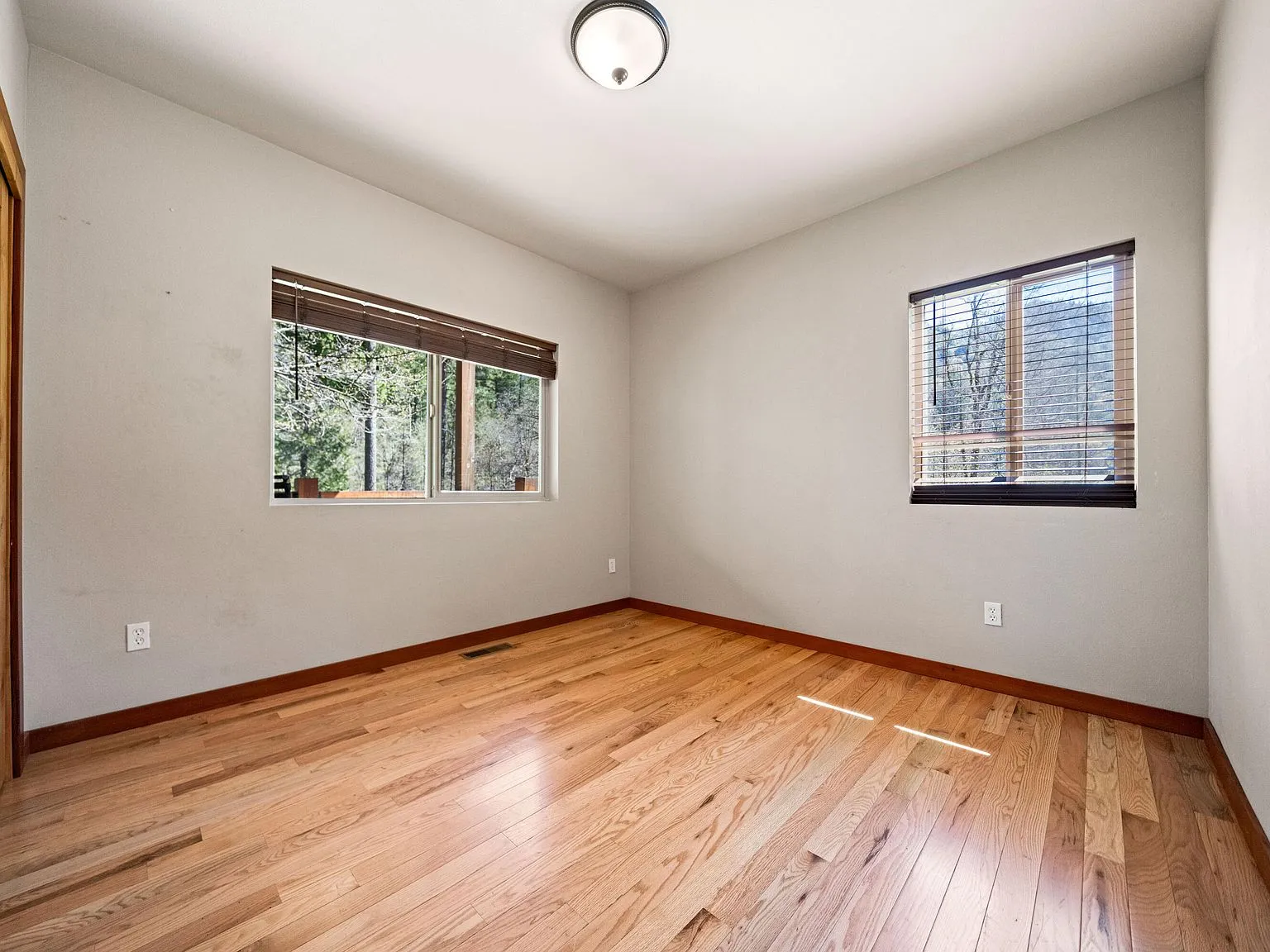 An empty bedroom with hardwood flooring and a window looking out at the trees