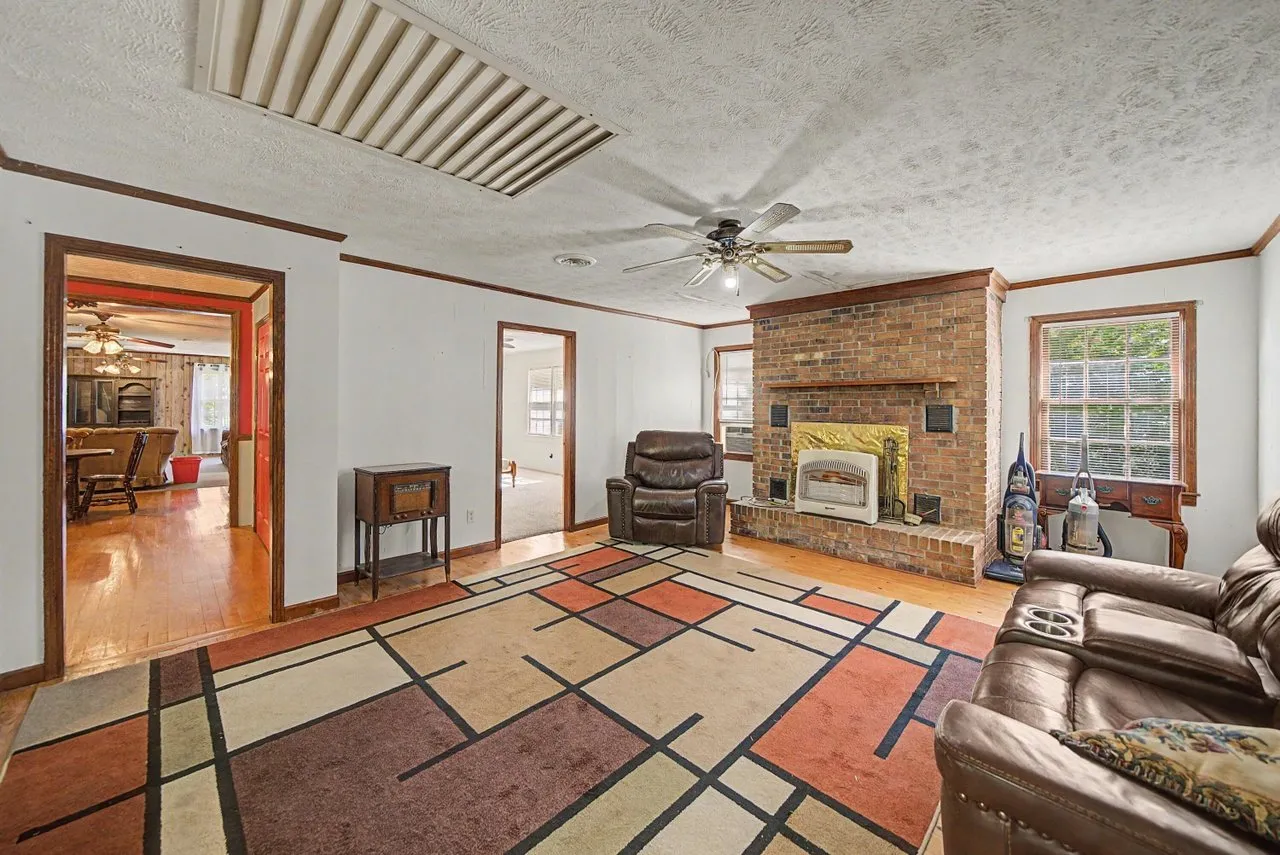 The living room with a brick fireplace, patterned rug and wood floors
