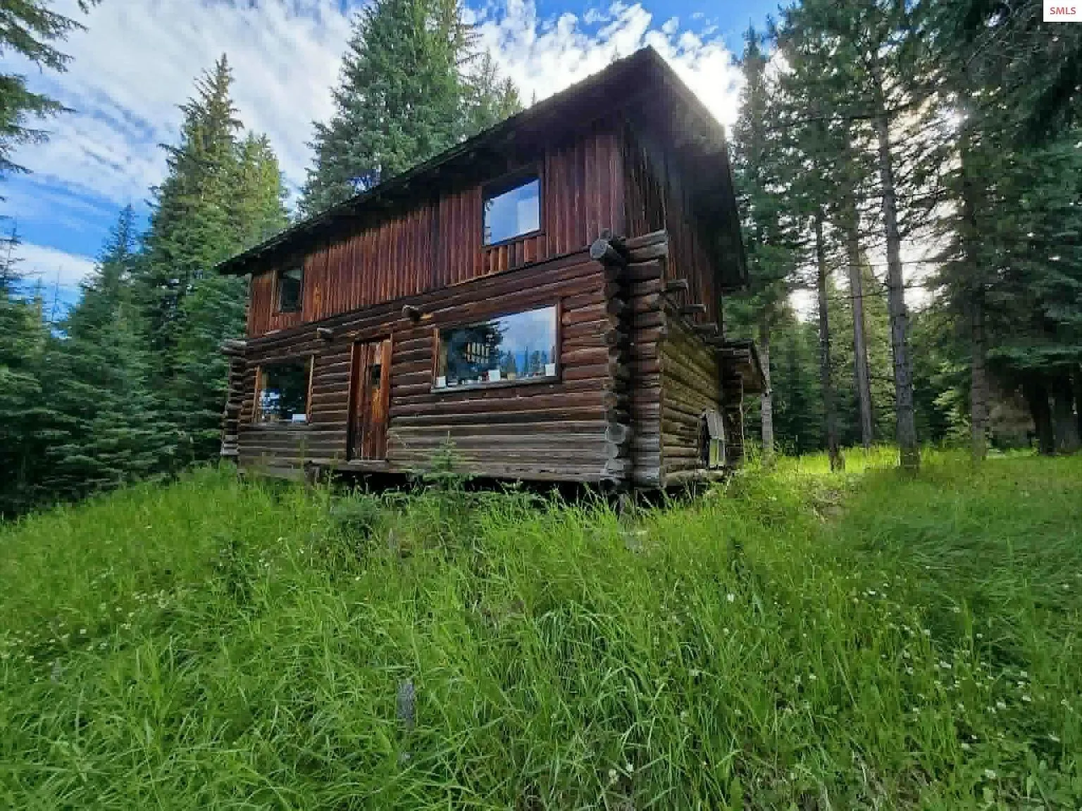 An upstairs bedroom with a bed frame, dresser and sloped log-paneled ceiling
