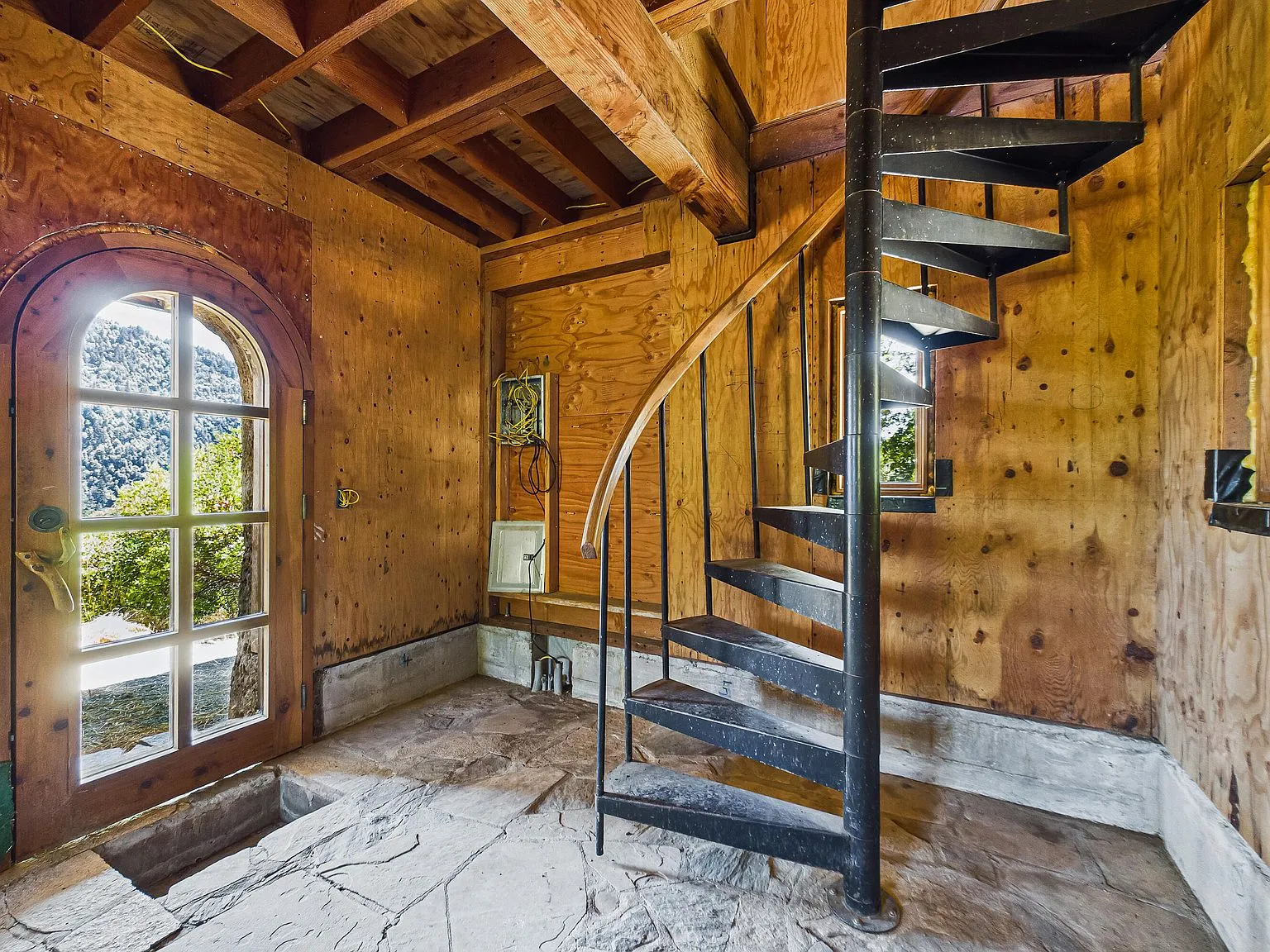 An unfinished room with exposed plywood walls and two windows overlooking the hills