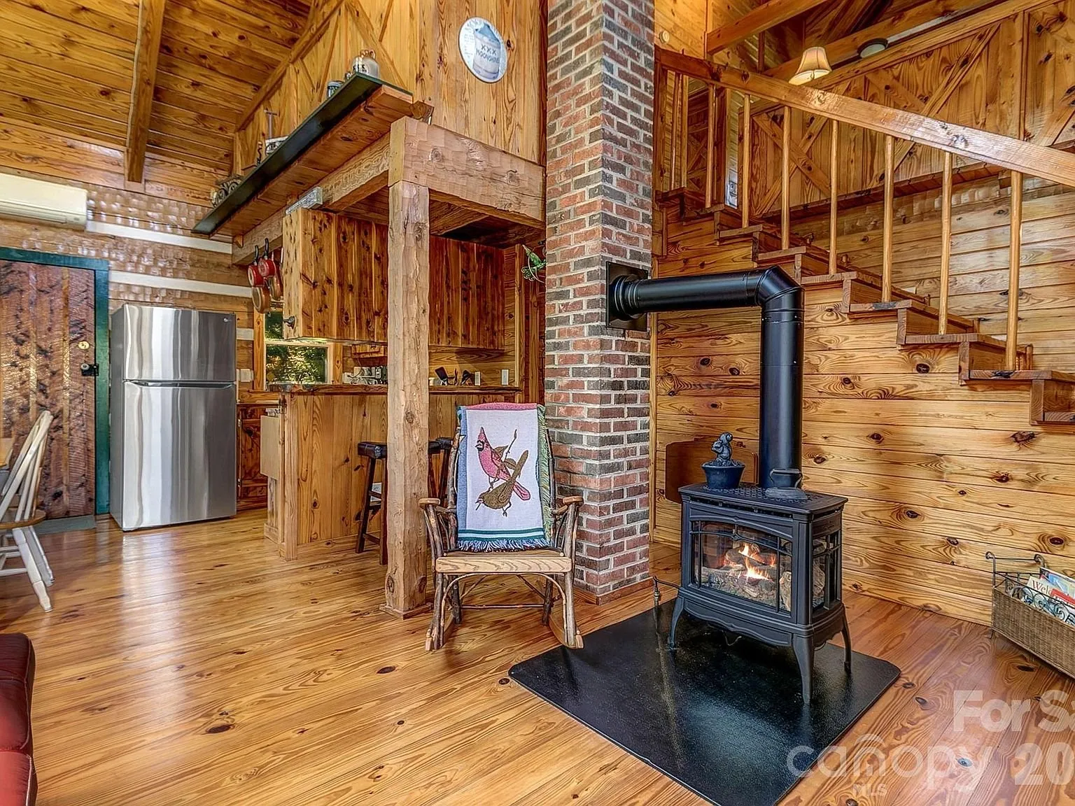 The two-story living room with the gas stove, a stone chimney and the stairs to the loft