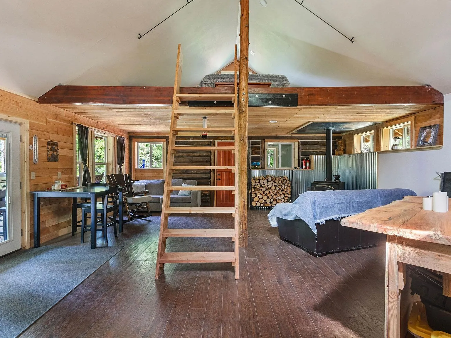 A central ladder rising through the cabin's vaulted, log-beamed ceiling to the loft