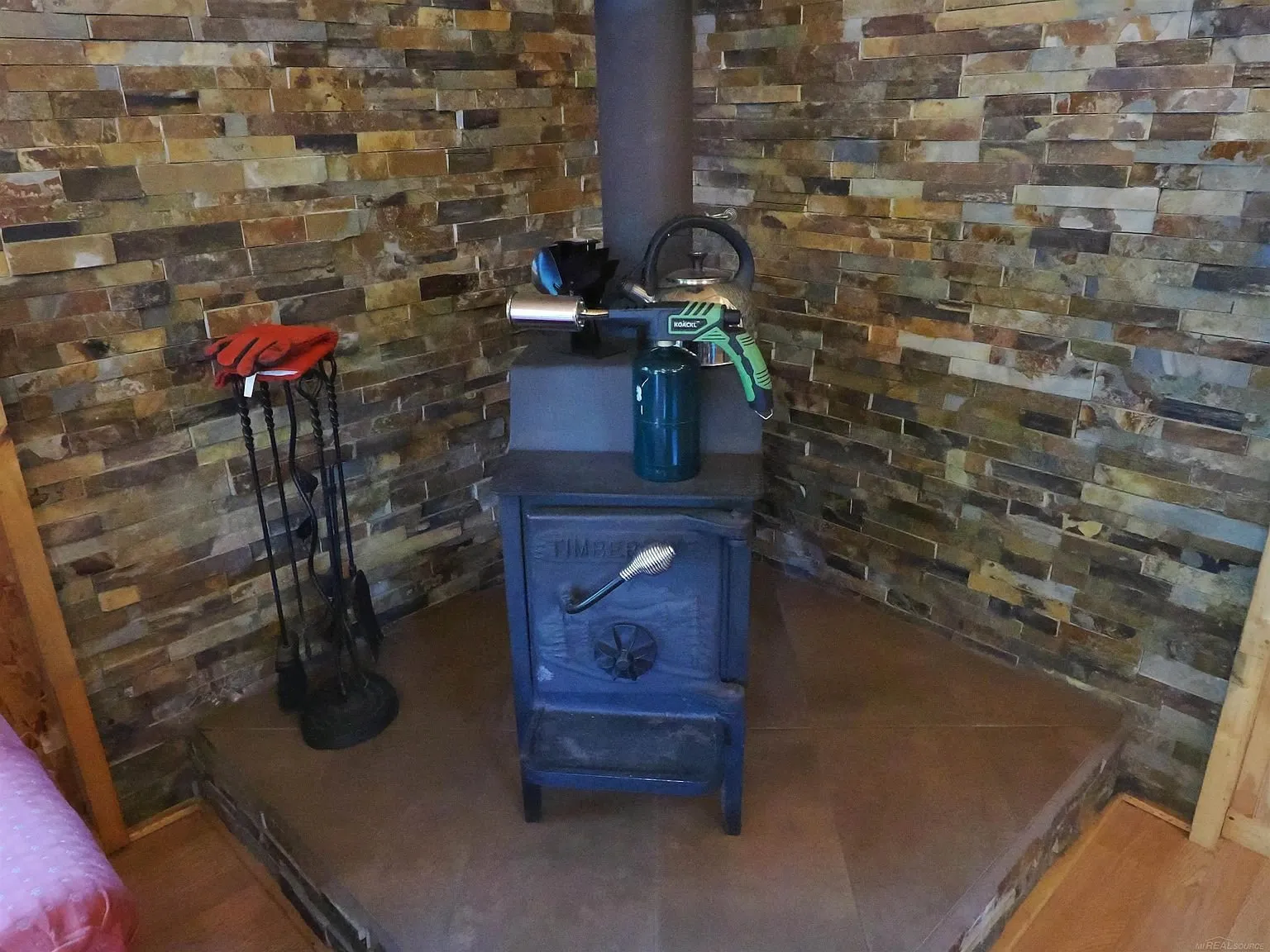 The wood stove on its hearth with the stone wall behind