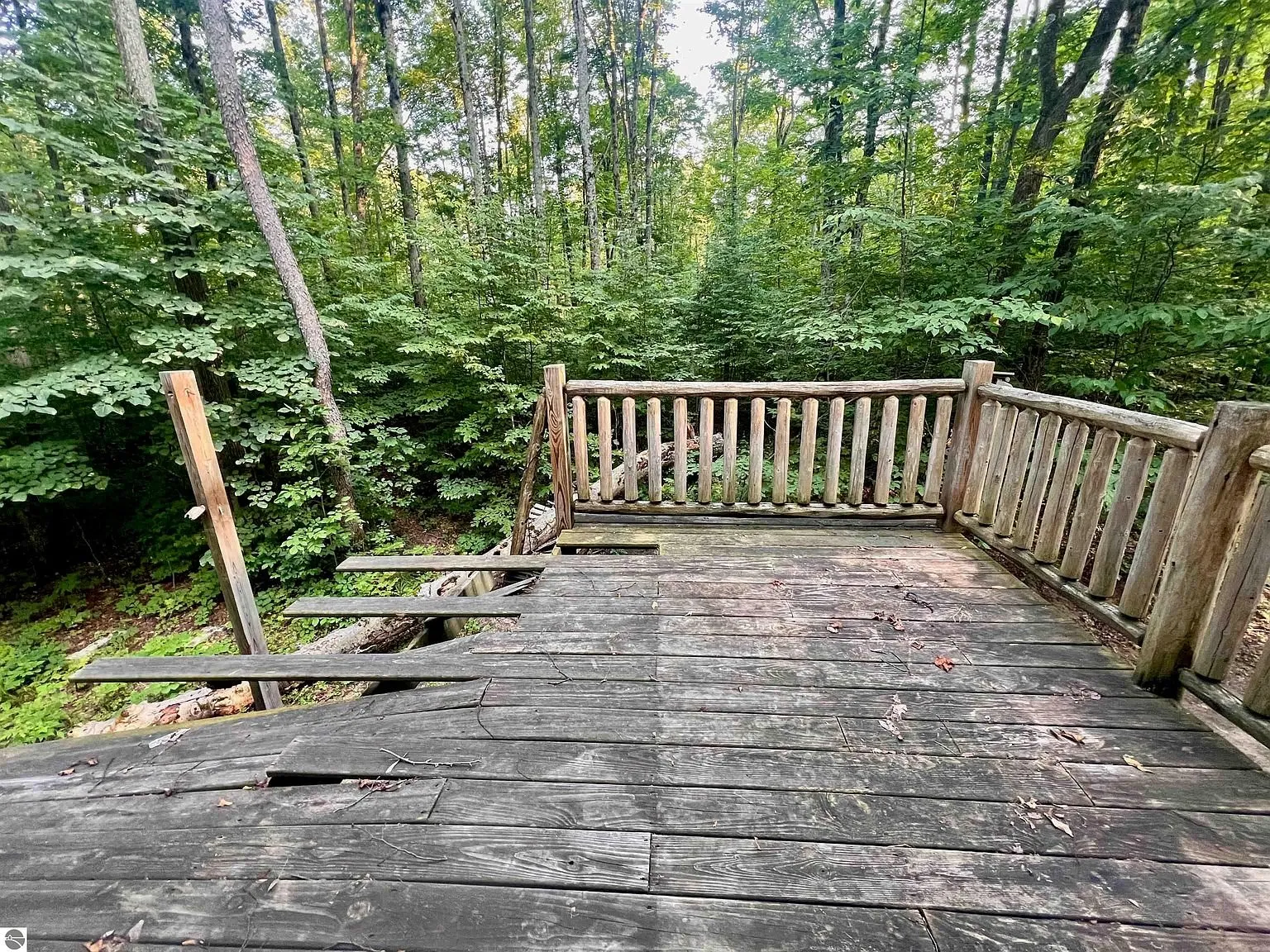The weathered deck boards of a balcony with the woods beyond