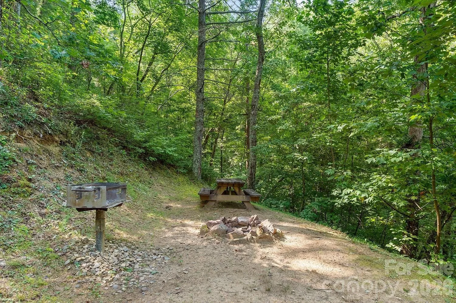 The fire pit, the picnic table and the grill on the bench below the slope