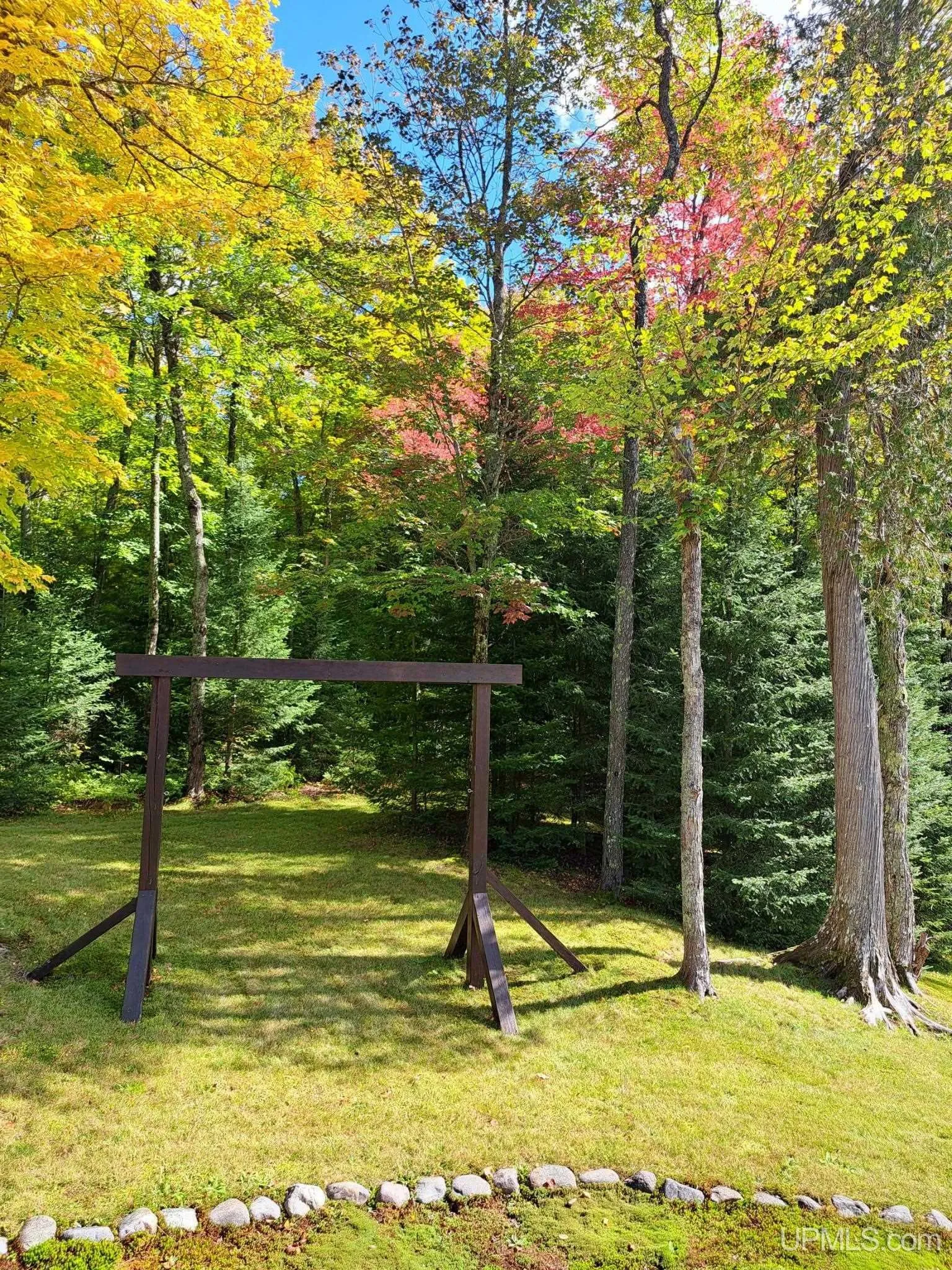 A swing set in the yard with autumn maples behind