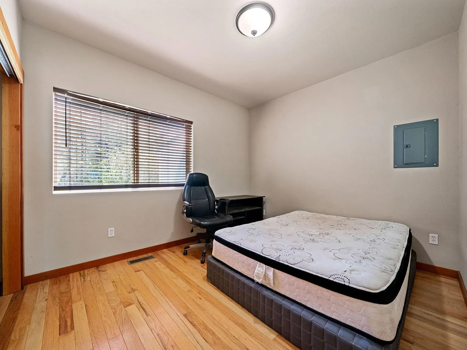 A second bedroom with a bare mattress and hardwood flooring