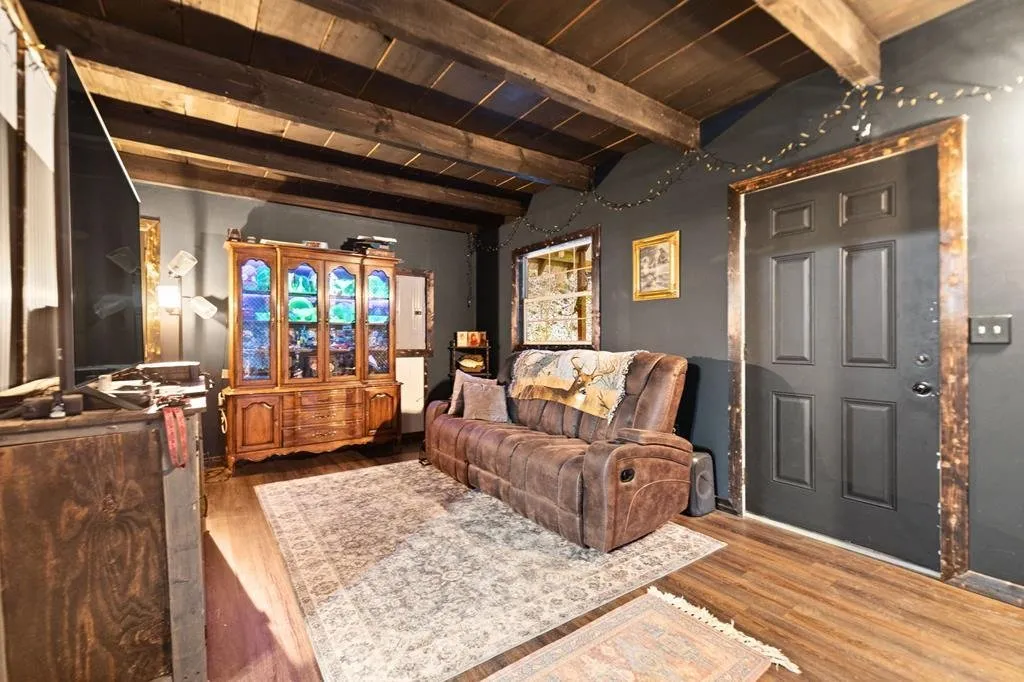 Living room with dark walls, a leather sofa, a wood cabinet and exposed beams