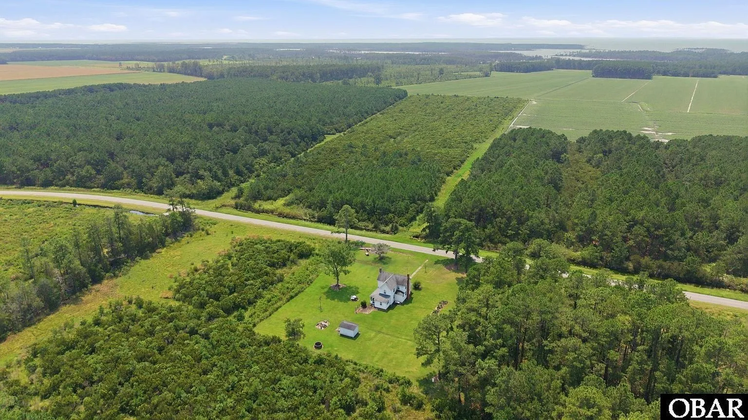 Aerial looking along Loop Road with the house in its clearing and fields beyond