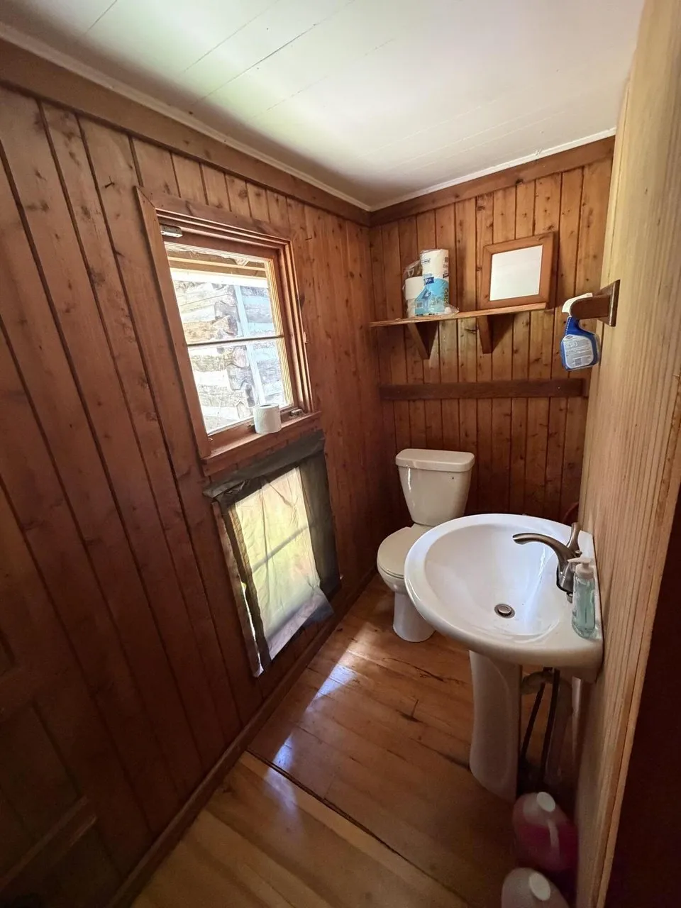 The bathroom in the spruce cabin with a pedestal sink and wood-paneled walls
