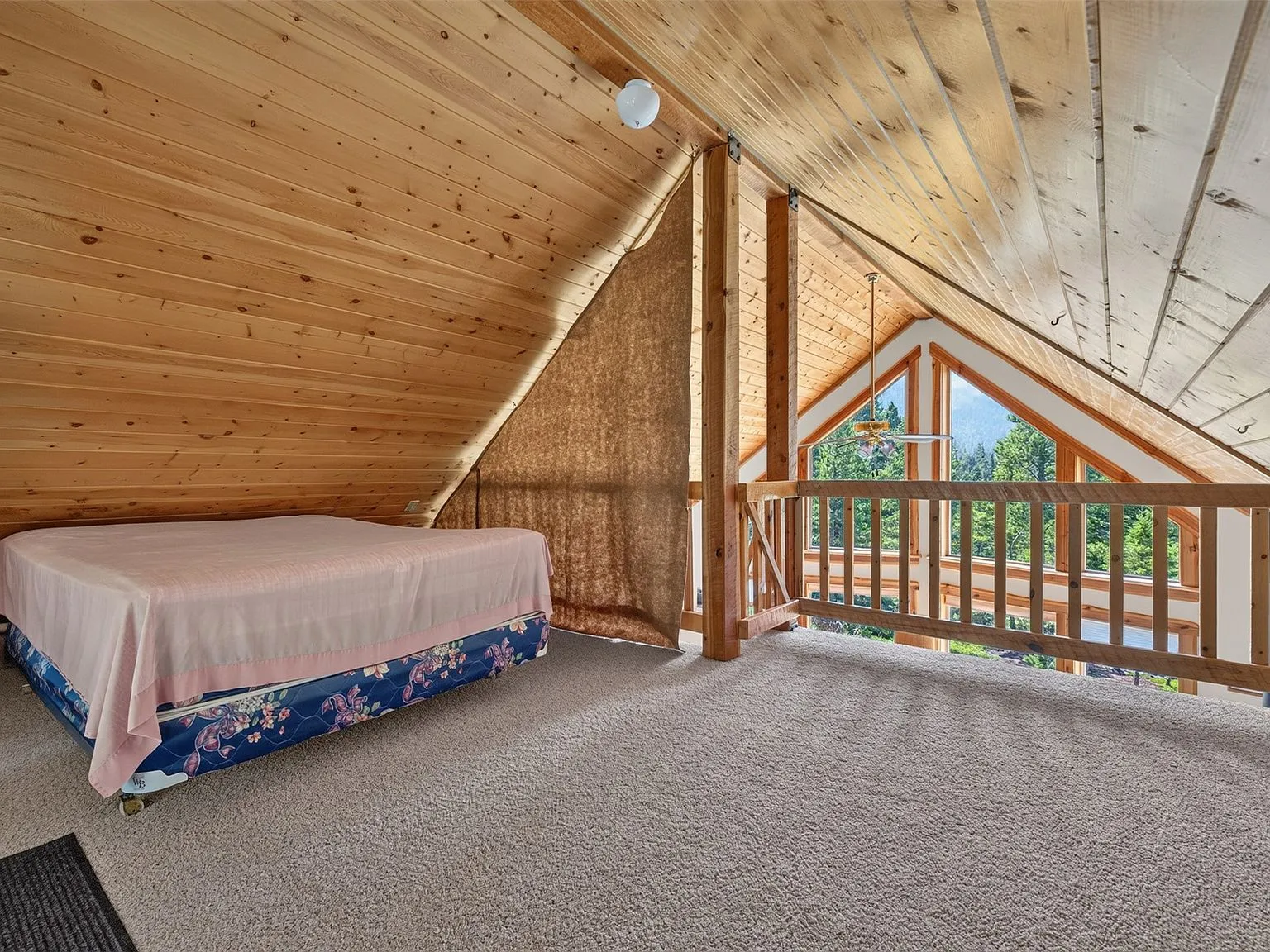A wide view of the loft's vaulted ceiling, triangular window and railing
