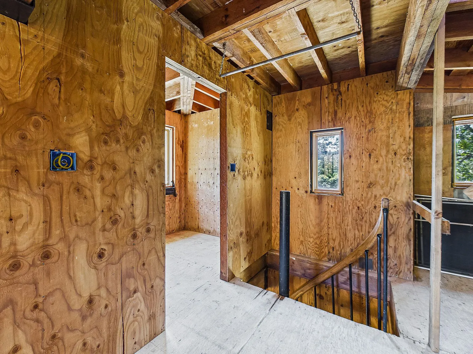 A hallway of exposed framing and plywood subfloor leading toward the home's interior