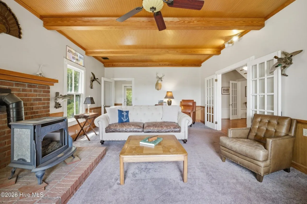 Family room with the wood stove on a brick hearth, exposed beams, and a ceiling fan