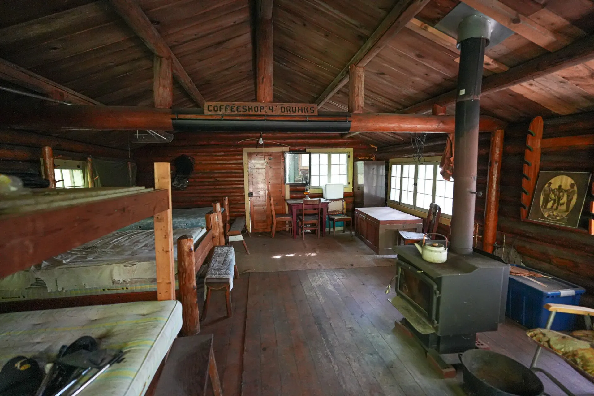 Inside the main cabin: bunks, a table, and a wood stove under the rafters