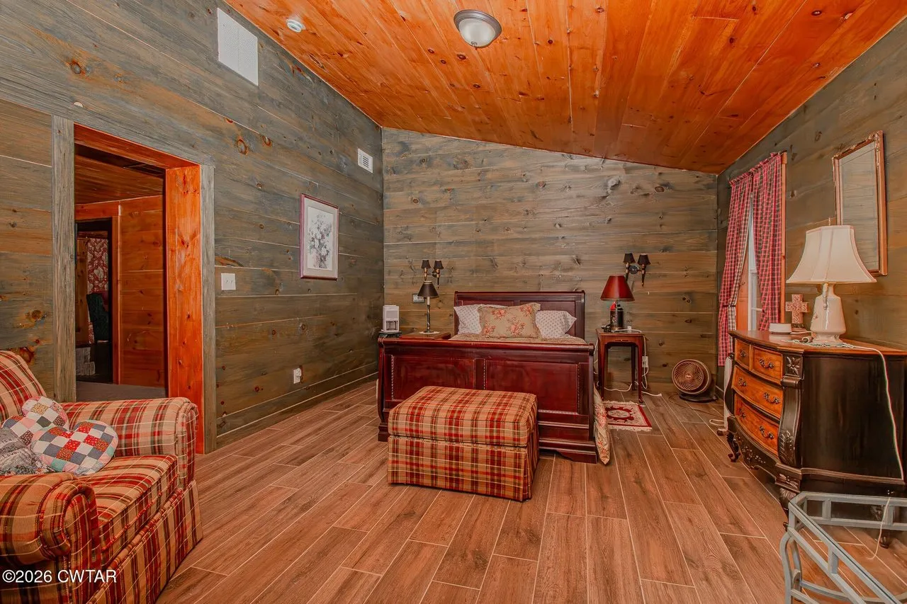 A bedroom with wood walls, a sleigh bed and a plaid armchair