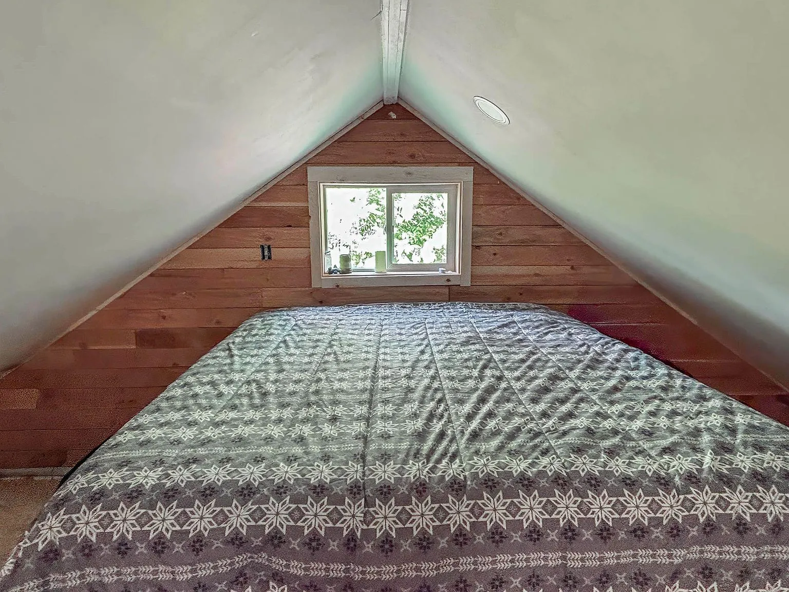 The peaked loft ceiling with a small window, set above a queen bed