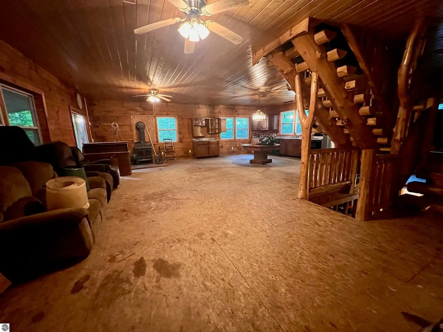 The great room with the log stair, the ceiling fans and the furniture along the wall
