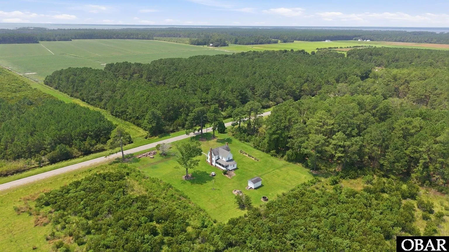 Aerial across the farm fields with the house at the edge of the pines