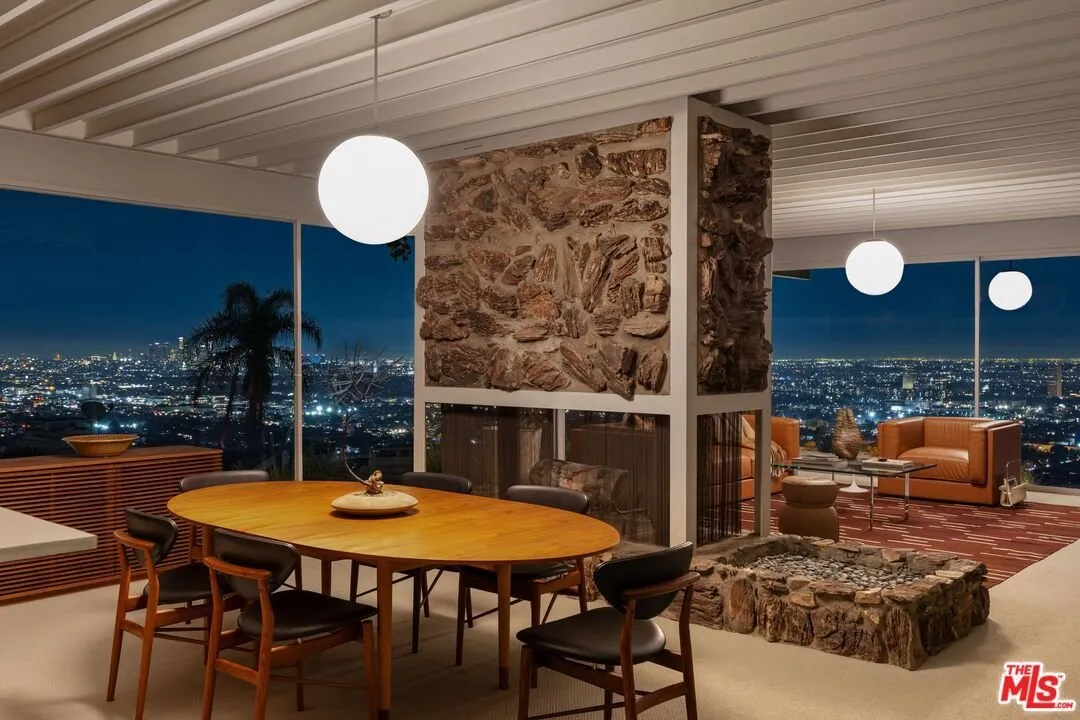 The dining table beside the stone fireplace column, city lights through the glass