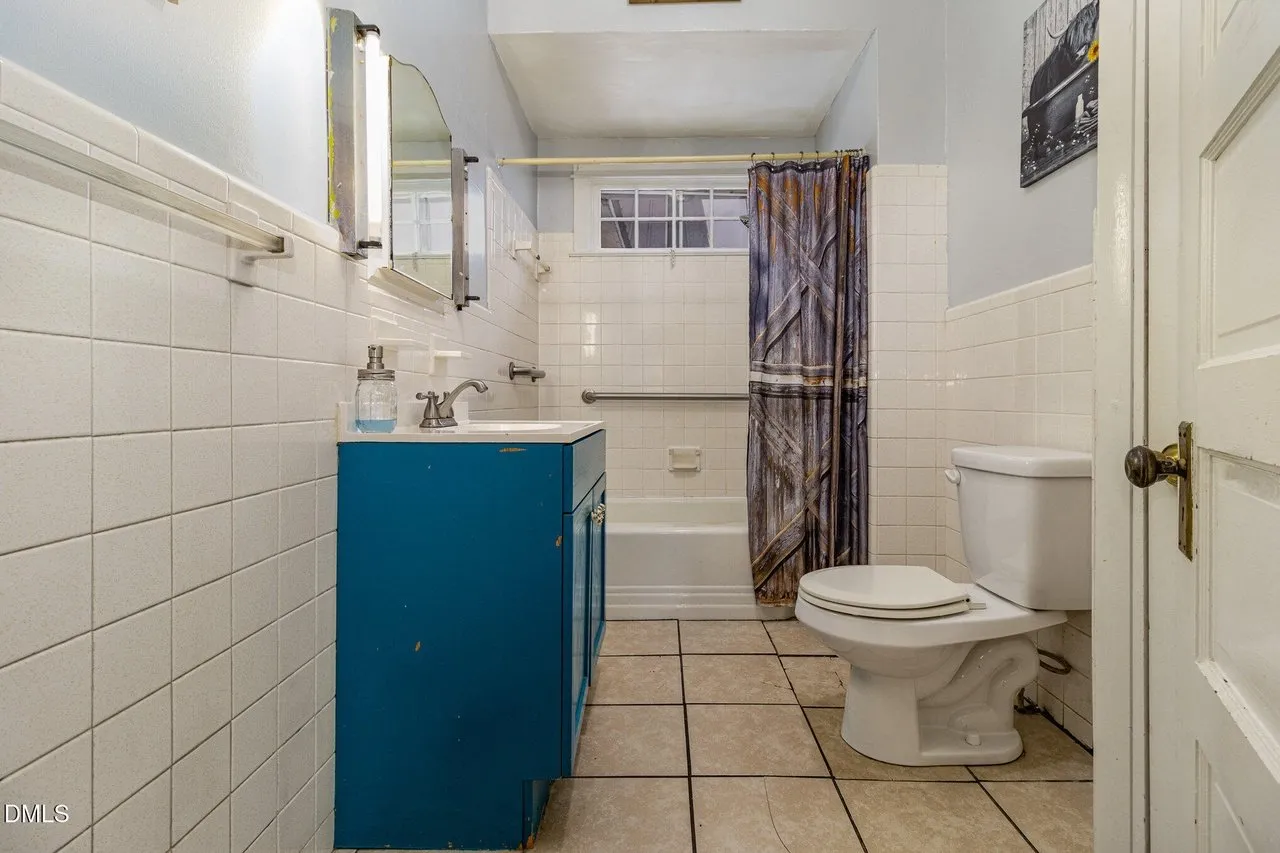 Bathroom with white tile, a teal vanity and a tub with a shower curtain