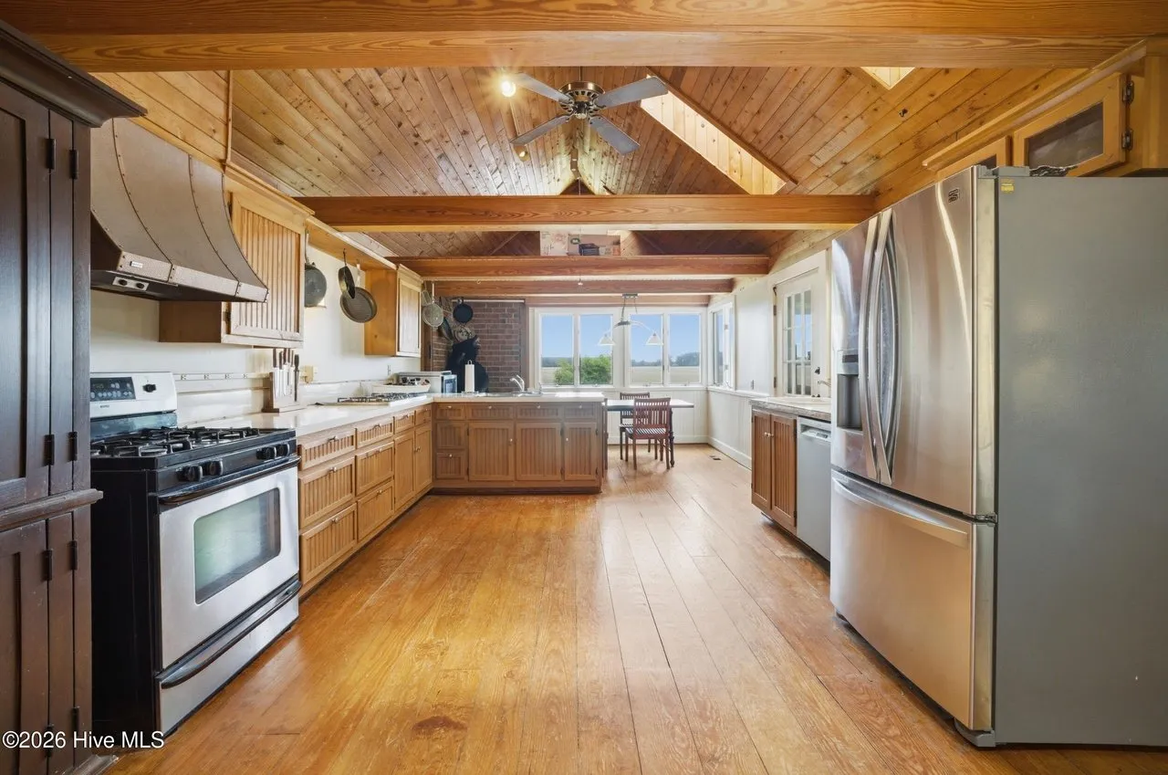 Kitchen with wood cabinets, a gas range, and a stainless refrigerator under a beamed ceiling