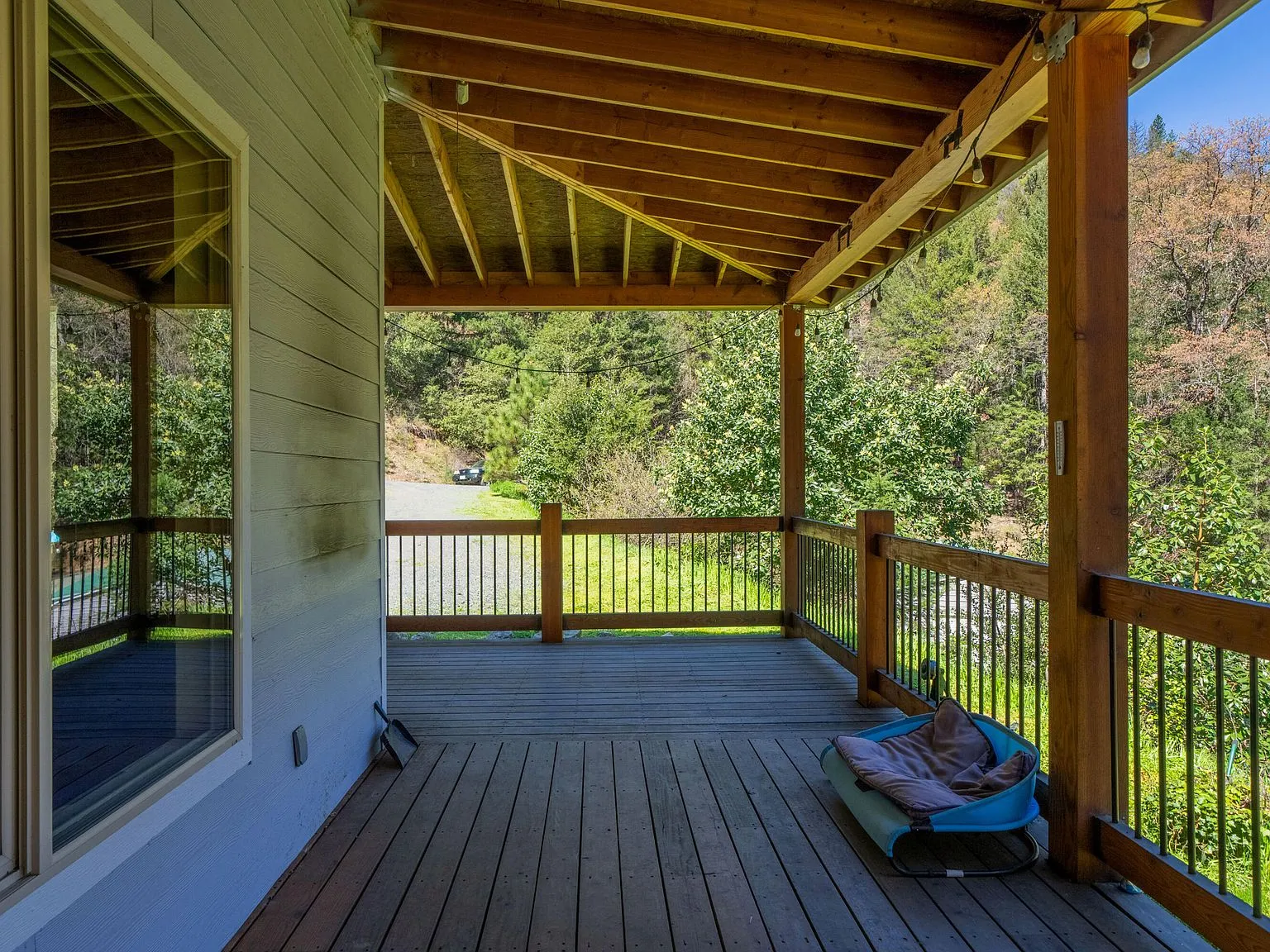 The covered wraparound deck with wood beam ceiling, overlooking the wooded yard