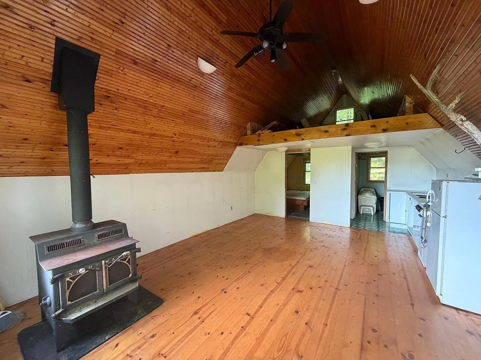 The main room with the wood stove, the ceiling fan and the refrigerator