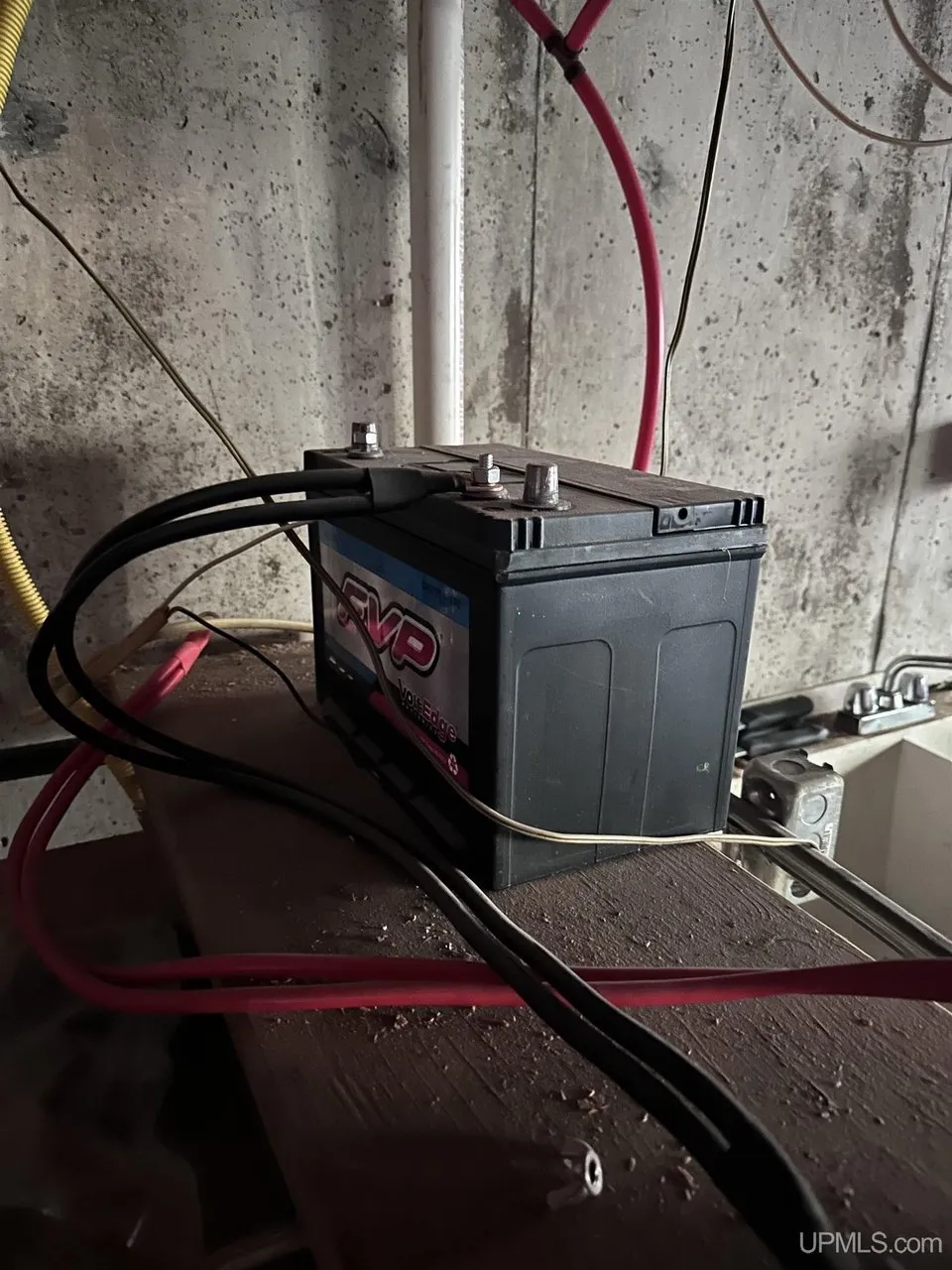 A single battery with heavy cables on a plank in the basement