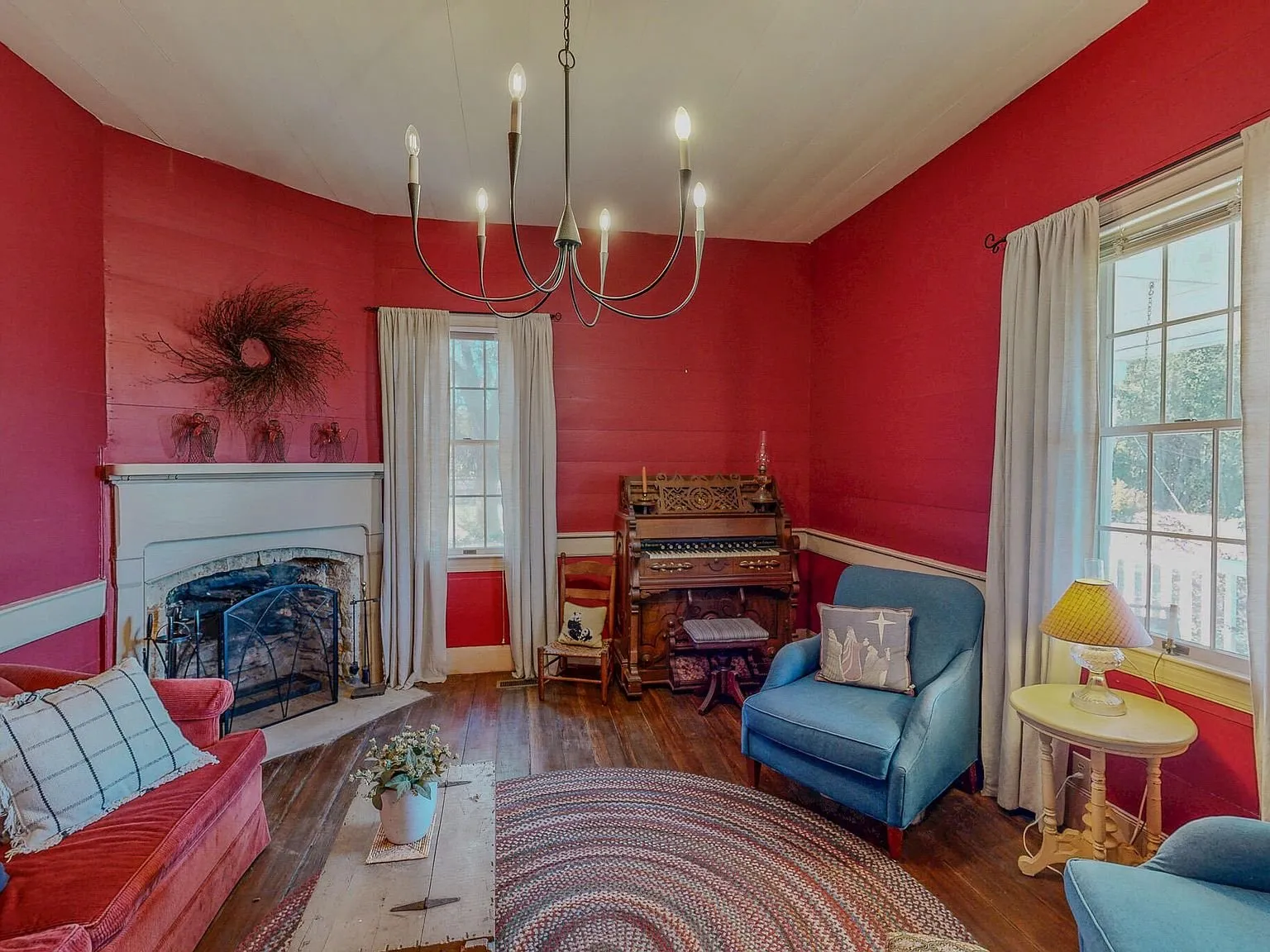 A red-walled parlor with a fireplace, a piano and blue armchairs