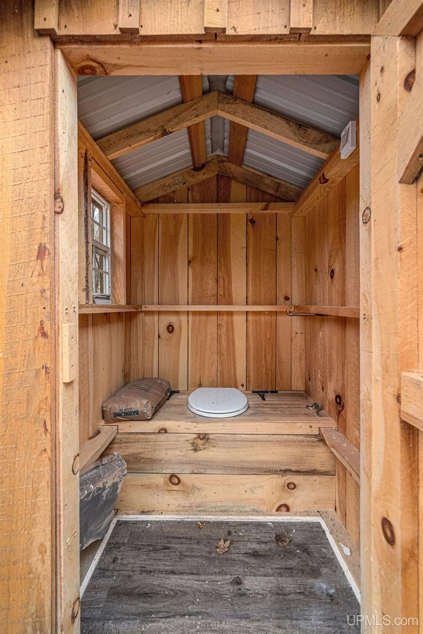 Inside the outhouse, a wooden bench seat under the pitched roof